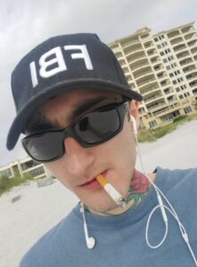 PHOTO Robert Crimo Wearing An FBI Hat Smoking Cigarette On The Beach