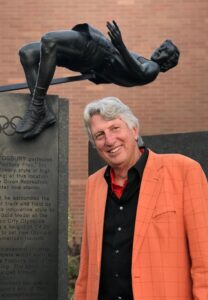 PHOTO Dick Fosbury In A Bright Orange Suit Posing For Picture Next To Olympic Statue