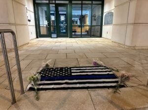 PHOTO Flag With Flowers Lying At The Steps Outside CMPD Headquarters In Uptown Charlotte As Tribute To Officer Joshua Eyer